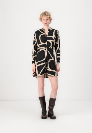 Robe noire avec des motifs abstraits beiges, manches longues, décolleté en V et taille à nouer. Finition avec des bottes marron au genou.