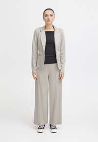Hellgrauer karierter Anzug mit taillierten Blazer und weit geschnittenen Hosen, kombiniert mit einem schwarzen Oberteil und schwarzen Sneakers. Glatte Textur, klassisches Design.