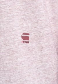 Ljusrosa sweatshirt i texturerat tyg. Har en liten bordeauxfärgad "RAW"-logotyp på framsidan, placerad till vänster om mitten.
