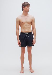 Ανδρικό μαύρο μαγιό σορτς με ελαστική μέση και κορδόνι. Ελαφρύ ύφασμα, σχεδίαση μέχρι το γόνατο, με απαλή υφή.