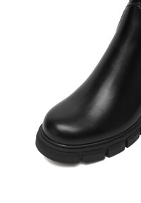 Cizme de gleznă din piele neagră cu talpă groasă și vârful rotund, prezentate pe un fundal alb.