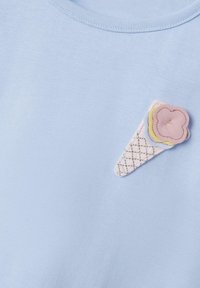 Camiseta de algodón azul claro con un aplique texturizado de cono de helado en colores pastel, con detalles bordados y un acento de flor rosa.