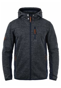 Chaqueta de forro polar gris oscuro con un panel lateral azul marino, bolsillos con cremallera, capucha ajustable y detalles en cuero marrón. Textura suave, estilo ajustado.