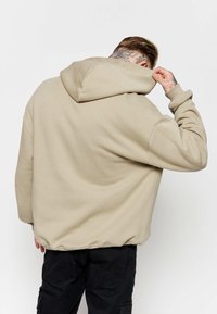 Sudadera beige con capucha de ajuste relajado, con una gran capucha, hombros caídos y puños acanalados, combinada con pantalones cargo negros.