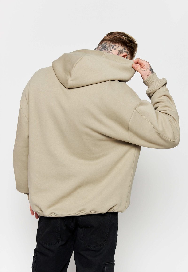 Sudadera beige con capucha de ajuste relajado, con una gran capucha, hombros caídos y puños acanalados, combinada con pantalones cargo negros.