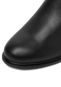 Čierna kožená členková čižma s elegantnou, zaoblenou špičkou, hladkou textúrou a jemným prešívaním pozdĺž okraja podrážky.