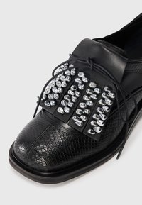 Black leather shoe featuring a textured snake pattern and metallic embellishments across the upper. Rounded toe and flat sole.