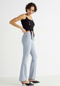Svart heklet crop topp med justerbare bånd, parret med lyseblå flared jeans. Modellen har på seg svarte spisse hæler.