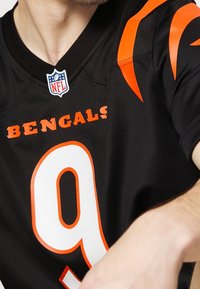 Czarny strój NFL z pomarańczowymi akcentami, wyraźnym napisem "BENGALS" oraz numerem "9" w wyraźnej białej obwódce. Klasyczny sportowy design.