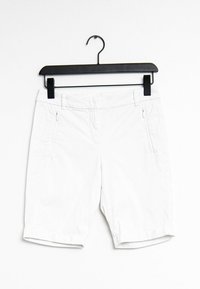 Shorts blancs en tissu léger, dotés de deux poches latérales zippées, d'un ourlet roulé et d'une texture lisse. Accrochés à un cintre noir.