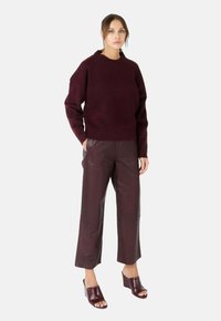 Bordeaux gebreide trui met ronde hals, gecombineerd met hoog-getailleerde bordeaux leren wijde broek en open teen bordeaux hakken.