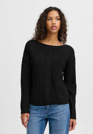 Black knitted sweater with a textured cable pattern, wide round neckline, and long sleeves, paired with light blue jeans.