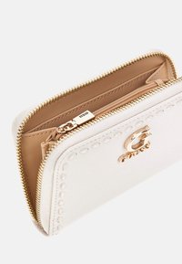 Portafoglio bianco in pelle con zip, hardware dorato, scomparti interni e motivo cucito lungo i bordi. Etichetta con logo visibile.