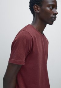 Karmesinrotes T-Shirt mit kurzen Ärmeln und Rundhalsausschnitt, aus einem strukturierten Stoff gefertigt, mit sichtbaren Nähten und lockerer Passform.