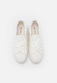 Baskets slip-on blanches en toile avec un design à l'avant noué, dotées d'une doublure à pois et d'une semelle en caoutchouc texturée.