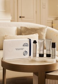 Set de regalo Rituals en caja blanca estampada con cinta azul marino. Contiene espuma de ducha, champú, loción corporal y desodorante, todos en tubos plateados.