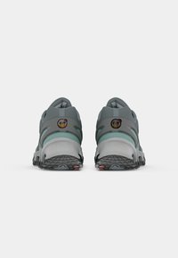 Gray athletic shoes with green accents, textured rubber soles, and a curved silhouette featuring circular logos on the heel.