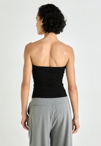 Top aderente nero senza spalline con superficie texturizzata, abbinato a pantaloni grigi a righe sottili. Inquadratura sulla vista posteriore, che mette in mostra una silhouette slanciata.
