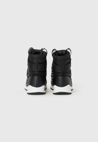 Par de botas de inverno pretas com parte superior acolchoada e solas brancas, apresentadas de trás sobre um fundo claro.