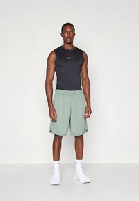 Musternik stiili must sleeveless sporditop, millel on valge Nike logo, koos heledate roheliste lühikeste pükstega. Komplekti lõpetavad valged spordijalatsid.