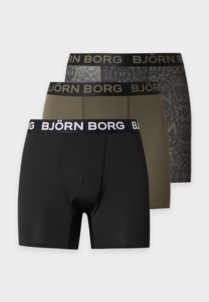 Homme torse nu, debout pieds nus, portant un boxer noir Björn Borg sur un fond clair uni.