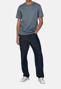 Helles blaues Baumwoll-T-Shirt mit Rundhalsausschnitt, kombiniert mit dunkelblauen Jeans. Weiße Sneakers runden das Outfit ab.