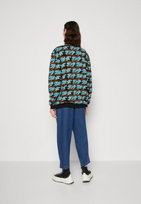 Kolorowa bluza z wzorem w niebieskie, pomarańczowe i czarne wzory, w zestawie z luźnymi niebieskimi dżinsami i czarnymi trampkami w stylu high-top.