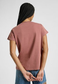 Camiseta de algodón de manga corta y cuello redondo en color rosa apagado. Presenta un corte relajado y recto, con detalles de costura mínimos en los dobladillos.