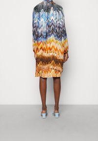 Långärmad klänning med ett chevronmönster i blå, orange och gula nyanser. Lättviktsmaterial med avslappnad passform, fållen når till mitten av låret.