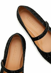 Bailarinas negras Mary Jane con textura brillante, forro de cuero y una correa en el empeine. Nombre de la marca "BALAGAN" grabado en la plantilla.