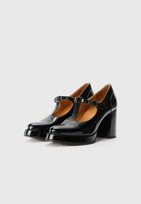 Chaussures à talons hauts en cuir noir avec une bride en T, bout arrondi, détails en cuir perforé et un large talon bloc pour plus de stabilité.