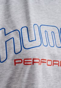Grå bomulls-T-shirt med stor blå text "HUMU" och röd text "PERFORMANCE", slät textur, rund halsringning och avslappnad passform.