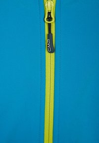 Giacca con zip in tessuto blu brillante, con una zip gialla a contrasto e un tirante nero con il marchio "CMP". Tessuto liscio.