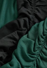 Fekete és zöld szövetrészek gyűrt textúrával. A fekete sötét és sima, míg a zöld enyhén fényes és puha.