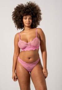 Kanten bralette en thong set in zacht roze. Beschikt over delicate scalloped randen en een bloemenpatroon. Dunne verstelbare bandjes.