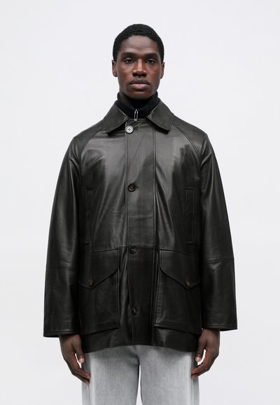 Melnās ādas jaka ar pogu aizdari, lielām priekšējām kabatām un apkakli. Iezīmējas teksturēts apdare un brīvs, pārmērīgs piegriezums.