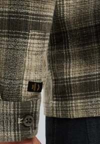 Geruite shirt in gedempte groene en beige tinten. Heeft een gestructureerde stof, knoopmanchetten en een zwarte label met "PME Legend" merknaam.
