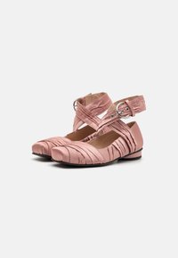 Pink satin ballet flats with ruched texture, rounded toe, and crisscross ankle straps featuring a metal buckle detail. Flat sole.