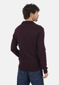 Bordeaux gebreide trui met een geribbelde textuur, voorzien van een klassieke kraag en lange mouwen, gecombineerd met blauwe spijkerbroeken.