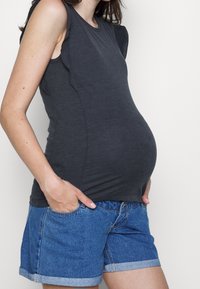Tmavě šedý, upnutý top bez rukávů s volánkovým detailem na rameni, kombinovaný s modrými denimovými šortkami. Hladká textura, neformální design a elastický materiál.