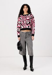 Maglione a maglia con un motivo a cuore rosa e nero, taglio crop, abbinato a jeans grigi a gamba larga, stivali neri fino al ginocchio e una borsetta nera lucida.