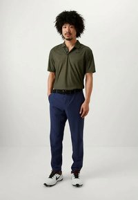 Maslinasto zelena polo majica s kratkim rukavima s suptilnim prugastim uzorkom, uparena s tamnoplave hlače i bijele tenisice. Crni remen naglašava odjevnu kombinaciju.