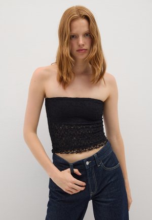 Top strapless de encaje negro con patrón floral texturizado, combinado con vaqueros oscuros de corte clásico y detalles en los bolsillos delanteros.