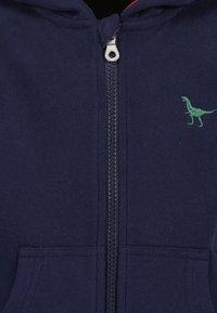 Dunkelblaue Zip-Hoodie mit grünem Dinosaurier-Stickerei auf der linken Brust und frontalen Taschen. Hergestellt aus weichem, bequemem Stoff.