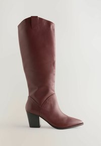 Burgundy nahkasaapas, jossa on terävä kärki ja kapeneva lohko korko. Siinä on sauma yksityiskohta ja vetoketju ylhäällä helpottamaan pukemista.