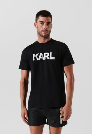 T-shirt in cotone nero con un grande logo bianco "KARL" sul petto e maniche corte, abbinato a pantaloni corti neri.