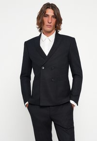 Blazer de doble botonadura en gris oscuro con tejido texturizado, solapas de pico y dos cierres de botón. Presenta bolsillos laterales y un corte ajustado.