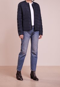 Padded black jacket with a round neckline, worn over a white t-shirt, paired with blue jeans and black heeled ankle boots. Minimalist design.