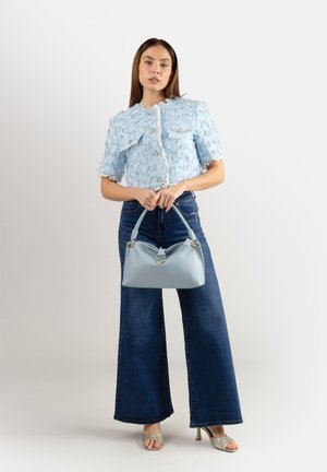 Donna che indossa una giacca a maniche corte azzurro chiaro con trama, jeans scuri a gamba larga, tiene una borsa azzurro chiaro e indossa tacchi argento con punta aperta.