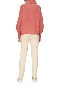 Rosa gestrickter Pullover mit hohem Kragen, oversized Schnitt; kombiniert mit beigen Hosen und Sneakers mit silbernen Akzenten. Rückansicht des Outfits.